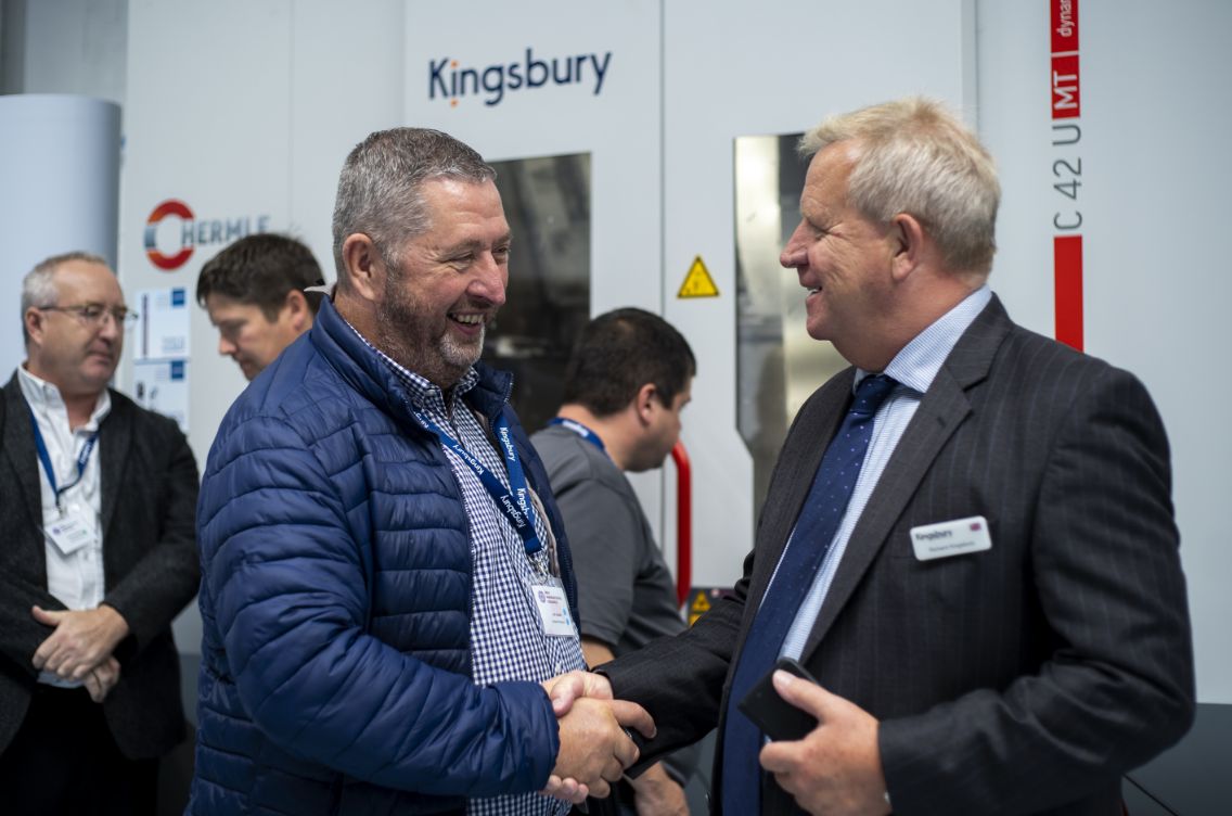 Richard Kingsbury shaking another mans hand next to Hermle machine