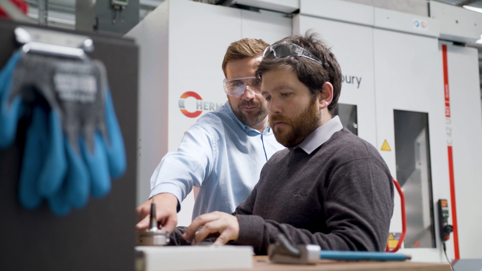 Two men working next to a Hermle machine