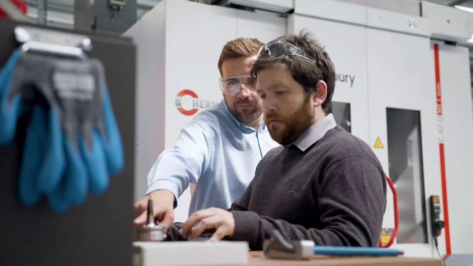 Two men working next to a Hermle machine
